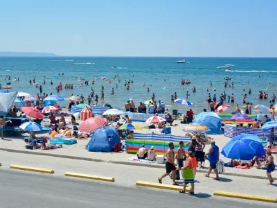 Crowds of people enjoying a sunny day at Wasaga Beach, with colorful umbrellas and families along the sandy shore.